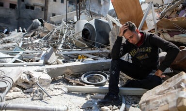 Man holding his head in hand sitting atop rubble