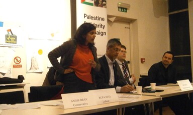 A woman stands and speaks at a table where others are seated