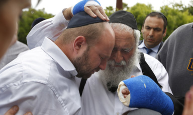Two men, one with bandaged hands, embrace, as others look on.