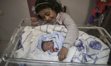 A little girl smiles at a newborn baby wrapped in a blanket.