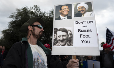 A man holds sign with pictures of Ilhan Omar and Hitler
