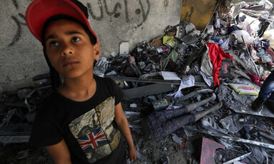 Boy stands in front of room filled with debris