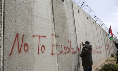 Man writes in red on an tall cement wall.