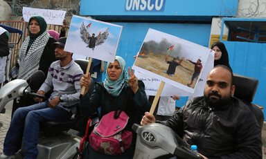 Man and woman using wheelchairs hold posters of double amputee holding Palestine flag
