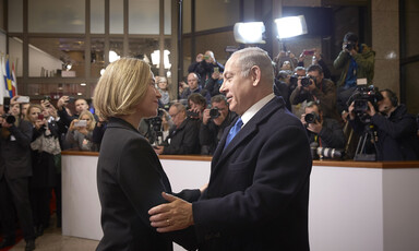 Man takes woman in his arms; people in the background watch on, many holding cameras.