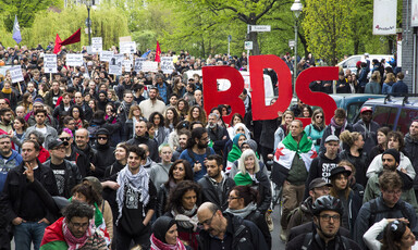 Hundreds of people march, some with signs that say "BDS"