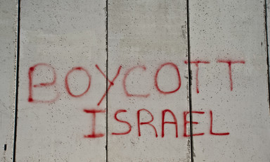 Graffiti written in red on a grey concrete wall reads, "Boycott Israel."
