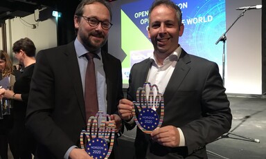 Two men smile and hold trophies that say "Horizon 2020"