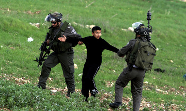 Two Israeli soldiers pull on the arms of a Palestinian youth.
