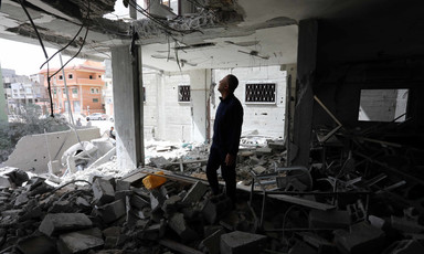 Man standing in bombed-out room looks up toward hole in ceiling