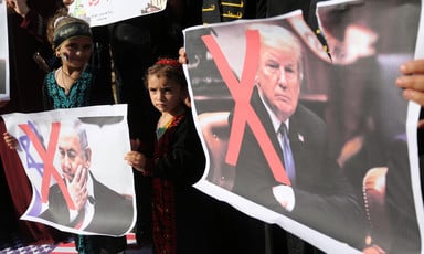 Girls hold signs with faces of Donald Trump and Benjamin Netanyahu crossed out.