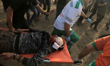 A man with a bandaged and bloody head is carried on a stretcher