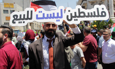Man wearing jacket and tie holding sign is seen from waist up
