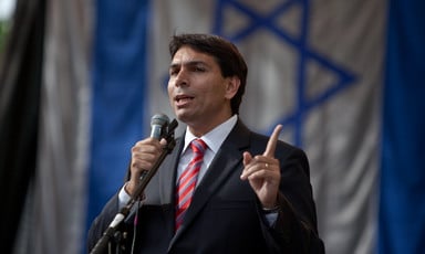 Man holds microphone in front of Israeli flag