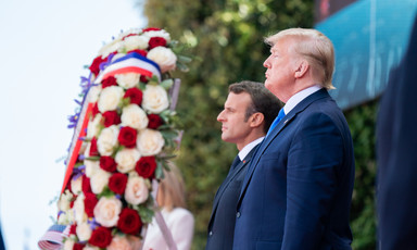 Macron and Trump stand beside a large wreath comprised of red and white roses 
