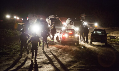 Armed police run in front of cars with the headlights on at night