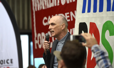 A man with a microphone addresses a crowd with signs