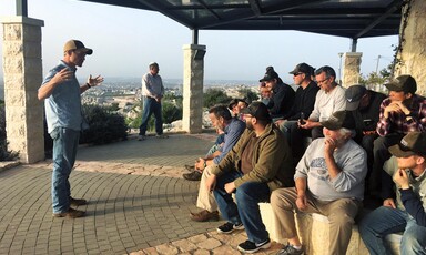 Men sit on a stone wall as another man gestures and speaks