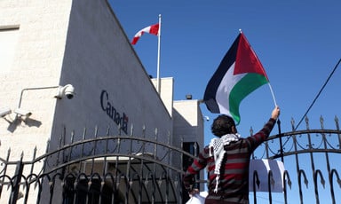 A protester waves a Palestinian flag over the gate of the Canadian mission in Ramallah.