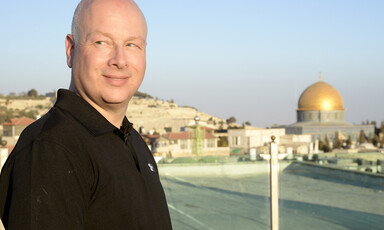 Man smiles with golden dome and other buildings behind him.