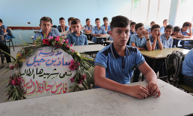 Boys sit in a classroom as a wreath with flowers and writing occupied one chair