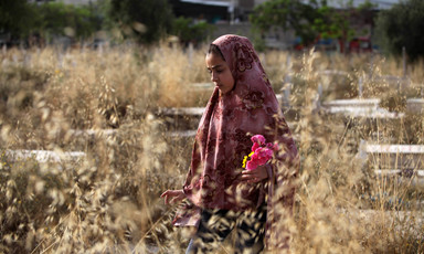 Woman wearing headscarf holds flowers in a wheat field