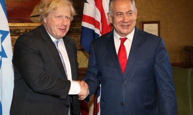 Two men shake heads in front of British and Israeli flags