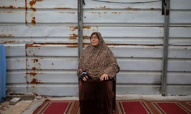 Woman sits in front of a wall, with a dark red rug beneath her feet. 