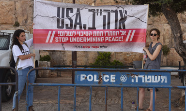 Two women hold sign reading "USA stop undermining peace" in English and Hebrew