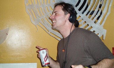 A man with headphones and a can of lager dances next to a record player