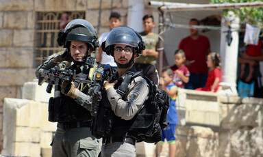 Two soldiers hold rifles in front of home