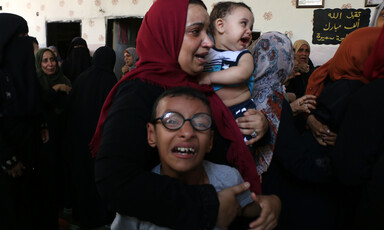 Woman embraces crying children in crowded room