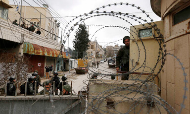 Soldiers seen behind barbed wire and walls with closed shops behind