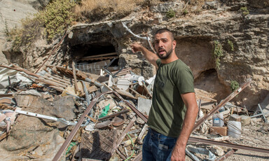 A man points to some rubble behind him