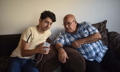 Two men share ear buds as they look at phone