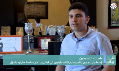 A young man sits in front of awards on a shelf.