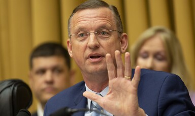 Man in blue suit holds up his hand. 