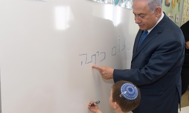 Man in suit looks over a child as he writes on whiteboard