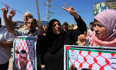 Palestinians hold banners, make peace sign with their hands