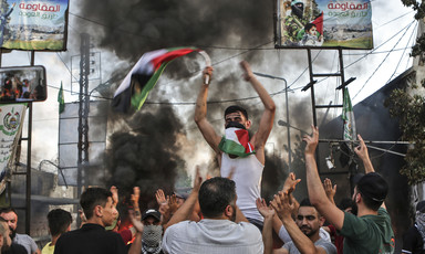 Man holding Palestinian flag carried by other men with backdrop of smoke