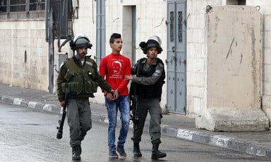 Two soldiers walk with handcuffed youth between them