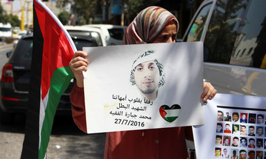 Woman holds Palestine flag and poster showing portrait of young man