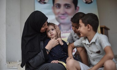 Woman cradles face of toddler as two older boys sit next to her