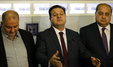 One besuited man, flanked by two others, gestures as he speaks.