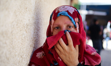 A woman holds a deep red veil up to her face.