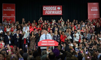 Man surrounded by crowd and signs speaks at podium