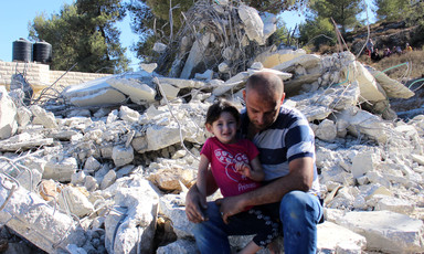 Man sits on rubble of a demolished home with young girl sitting on his leg