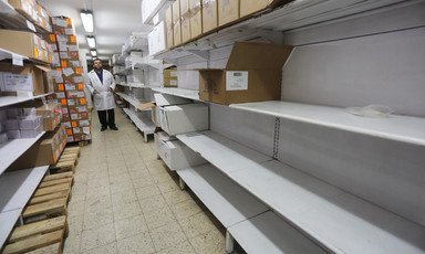 Man stands behind shelves, many of them empty. 