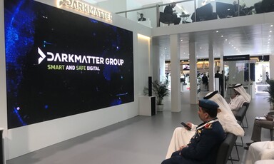 Men sit on chairs facing giant screen