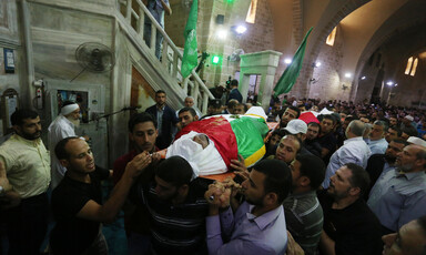Men carry two dead bodies covered by shrouds and flags. 